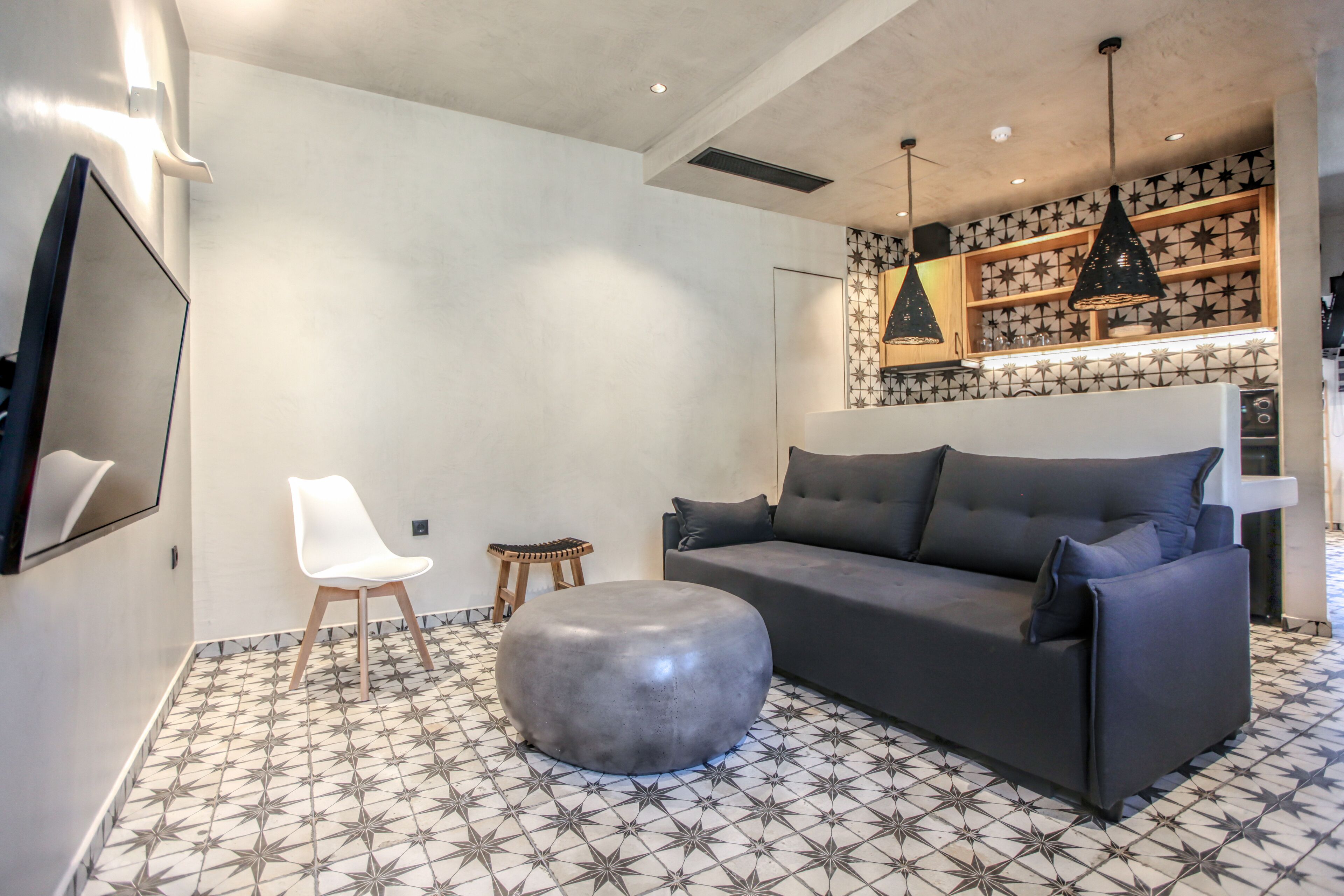Ein modernes Wohnzimmer mit grauem Sofa, einem weißen Sessel und einem runden Hocker auf einem gemusterten Boden.