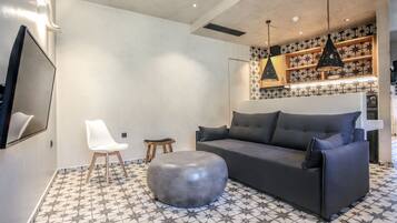 Ein modernes Wohnzimmer mit grauem Sofa, einem weißen Sessel und einem runden Hocker auf einem gemusterten Boden.