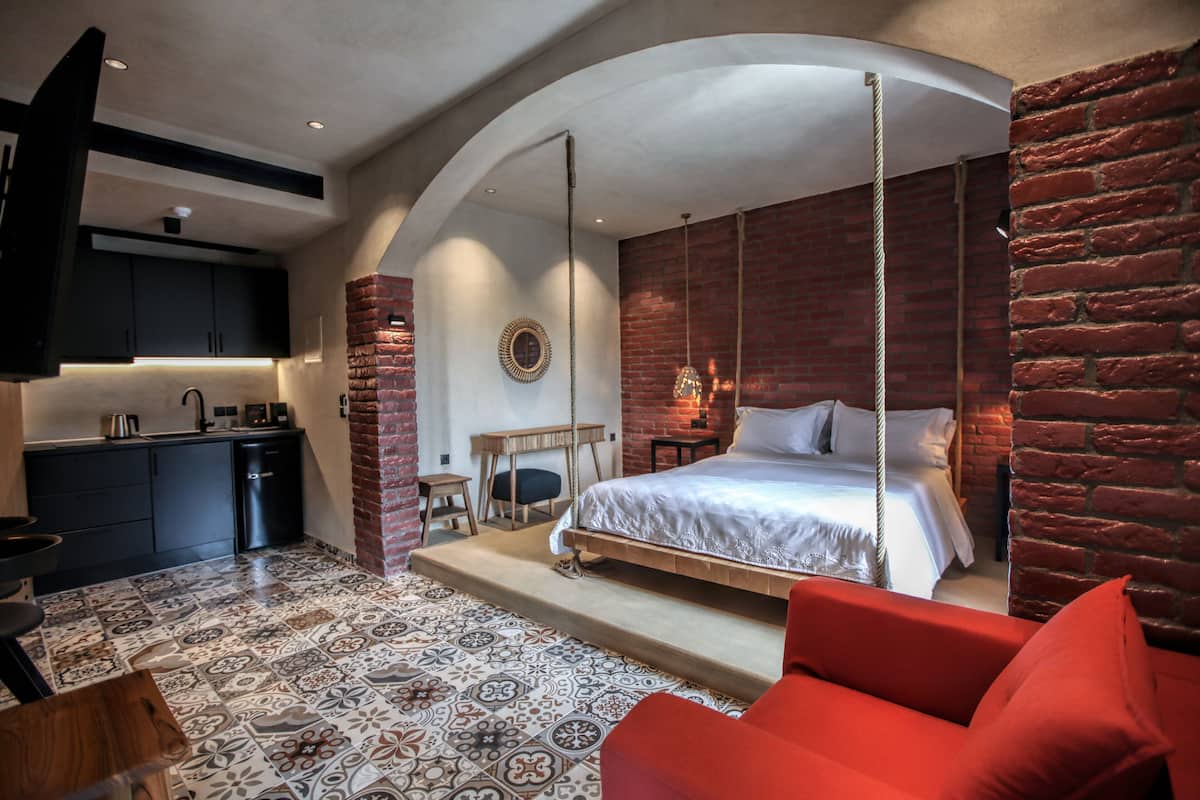 A modern bedroom with a hanging bed, a kitchen area, and a red sofa.