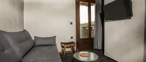 A modern living room with a grey sofa, a small wooden stool, a round metal table, and a TV mounted on the wall.
