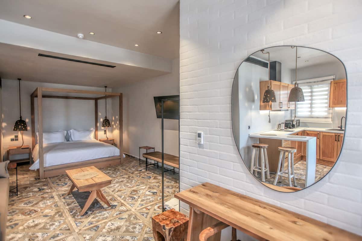 A bedroom with a bed, bedside tables, a mirror, and a view into a kitchen area.