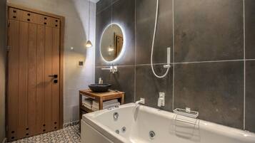 A modern bathroom with a freestanding bathtub, a wooden door, a round mirror, and a small wooden vanity with a bowl sink.