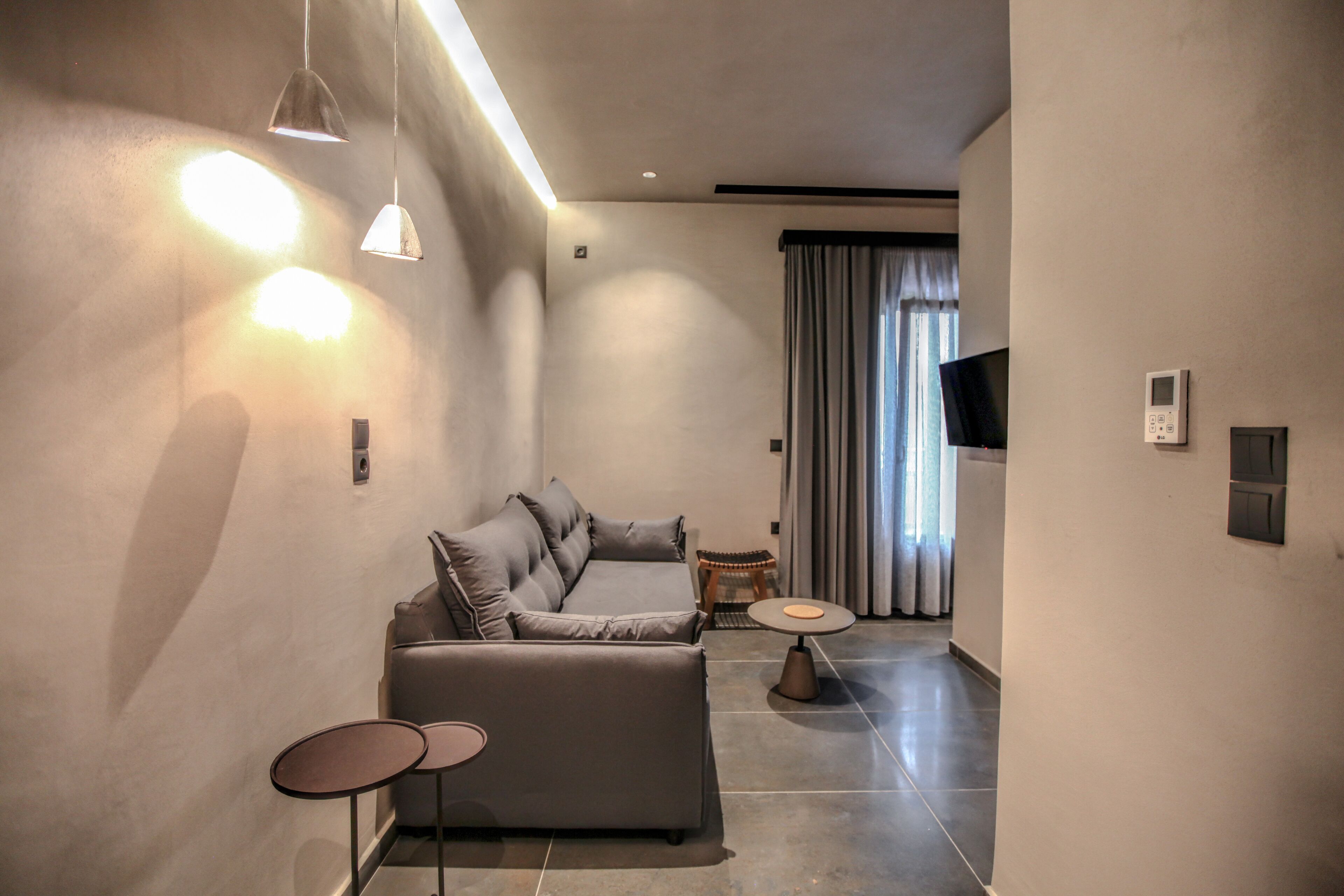 Una sala moderna con un sofá gris, dos mesitas redondas e iluminación colgante.