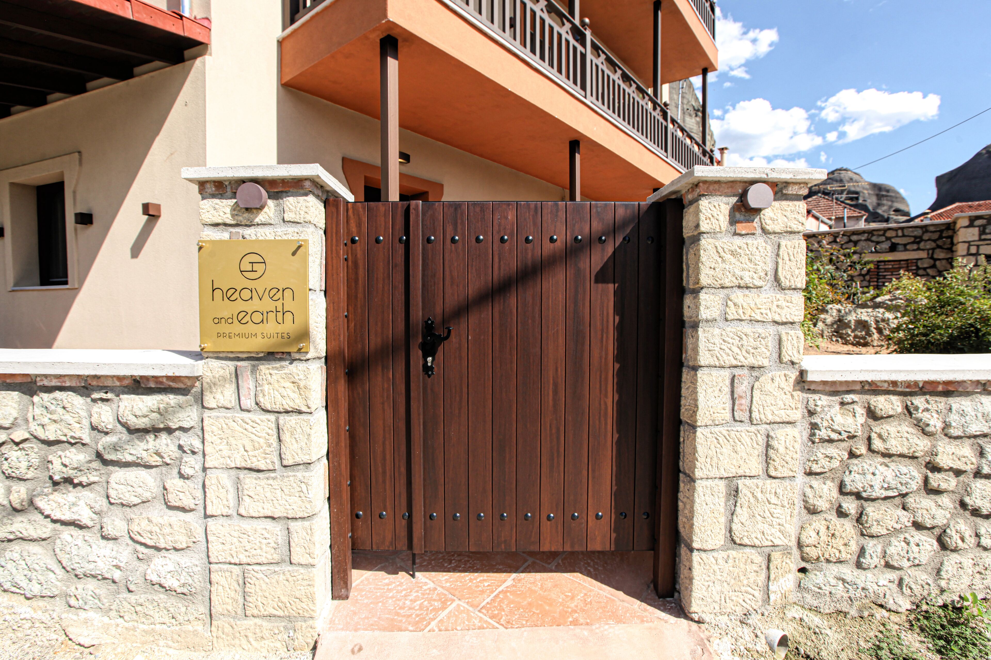 A gated entrance to a building with a stone wall and a wooden gate. A sign on the wall reads "Heaven and Earth Premium Suites."