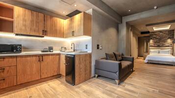 Una cocina moderna con armarios de madera y un microondas integrado. Hay un sofá gris y una cama en la habitación contigua.