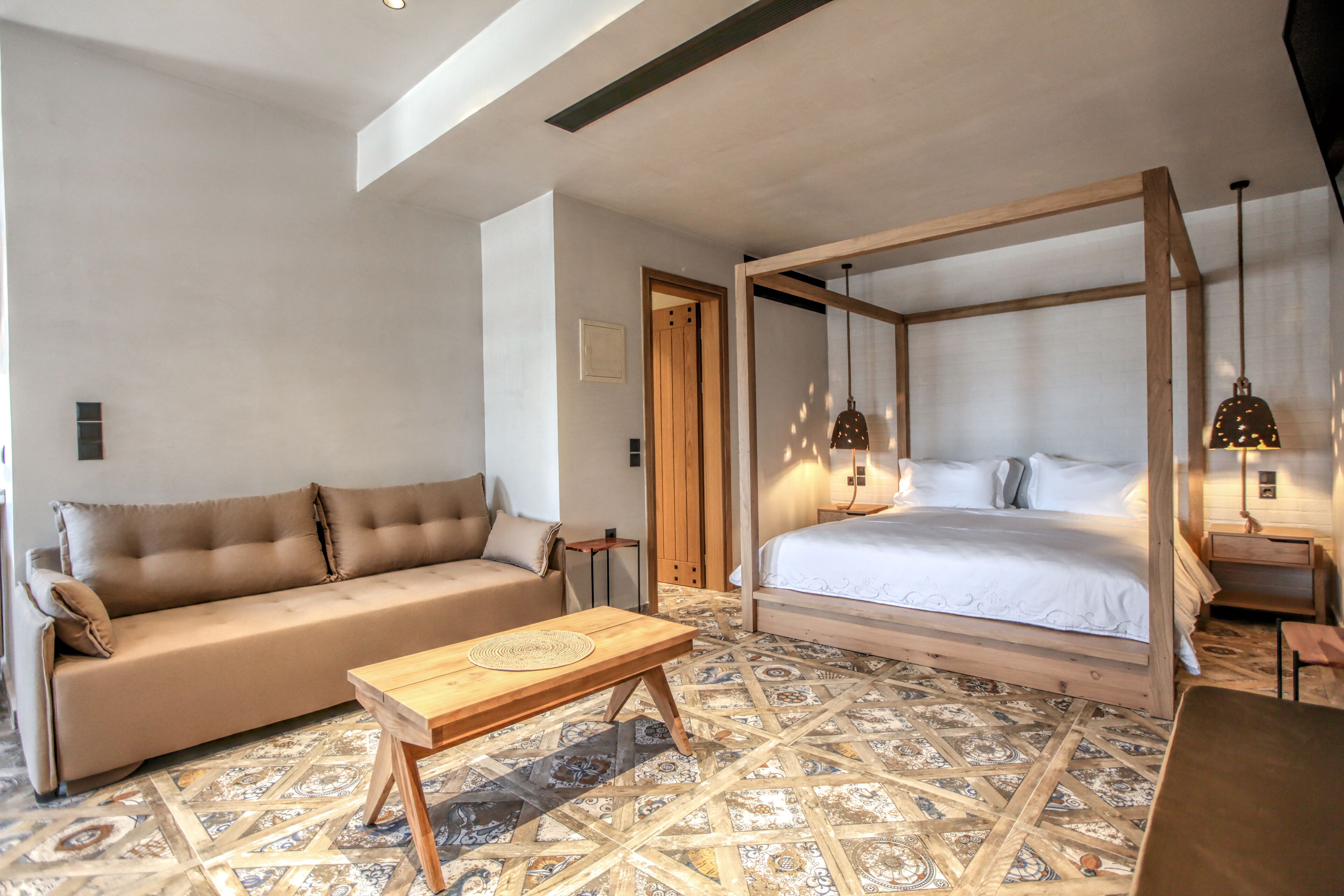 A bedroom with a four-poster bed, a sofa, a wooden coffee table, and patterned flooring.