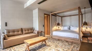 A bedroom with a four-poster bed, a sofa, a wooden coffee table, and patterned flooring.