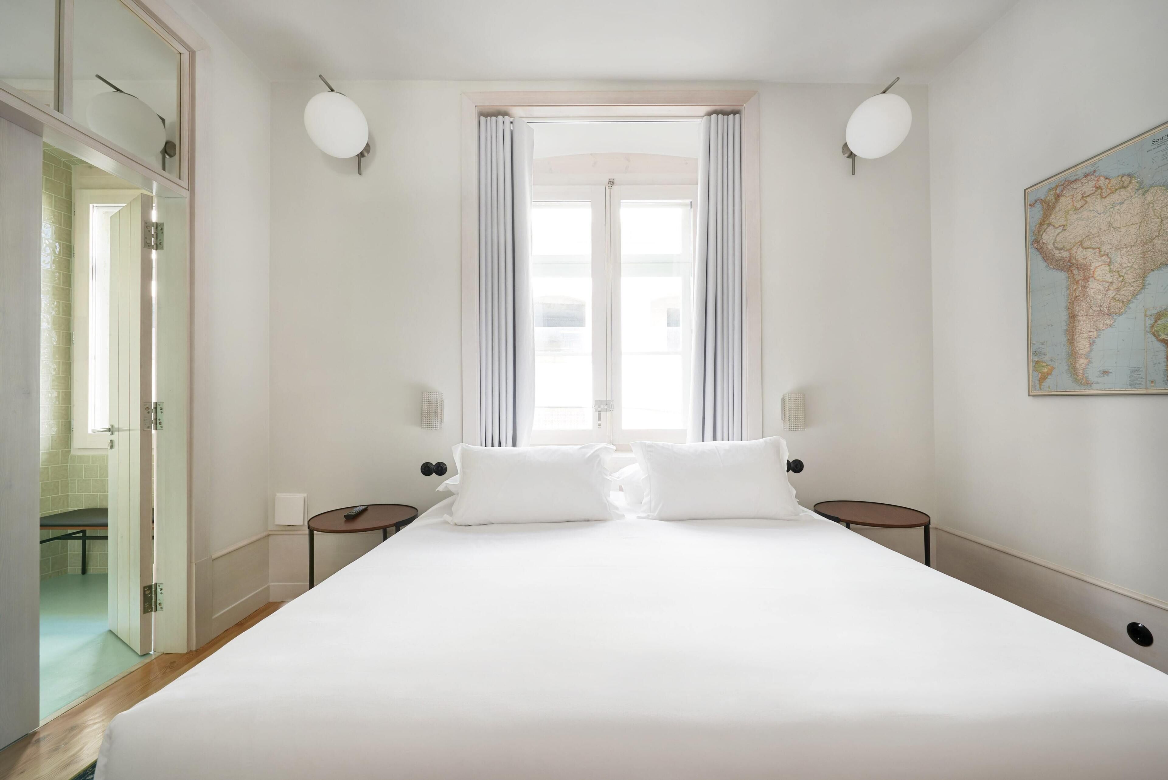 Ein geräumiges Schlafzimmer mit einem großen Bett, zwei Nachttischen, einem Fenster mit Vorhängen und einer Karte an der Wand.