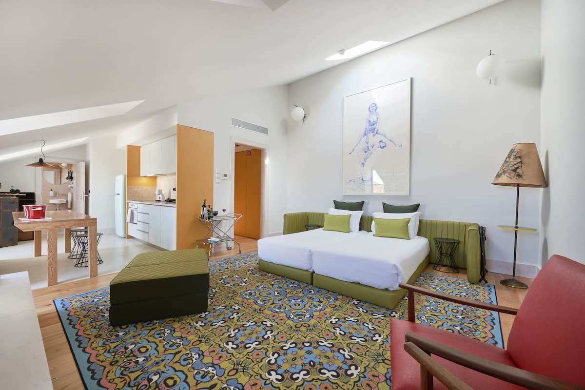 Una habitación de hotel moderna con una cama grande, un escritorio, una kitchenette y una alfombra colorida con estampado.