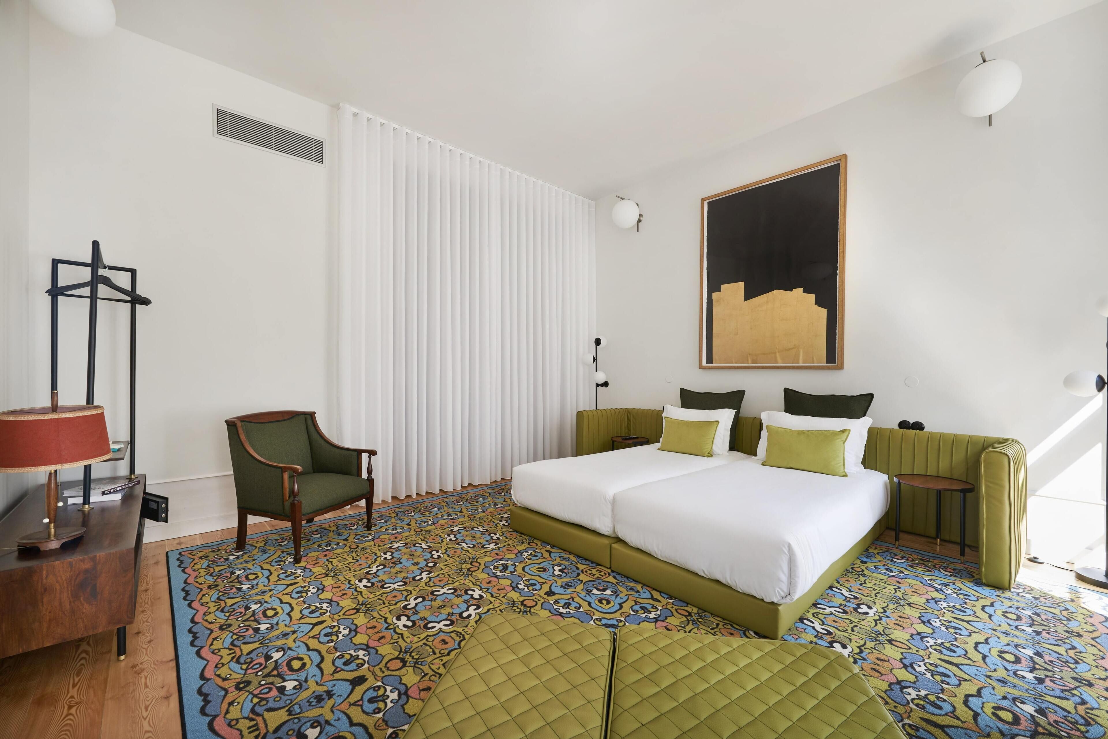Ein Hotelzimmer mit einem Bett, einem Sessel, einem Schreibtisch und einem gemusterten Teppich.