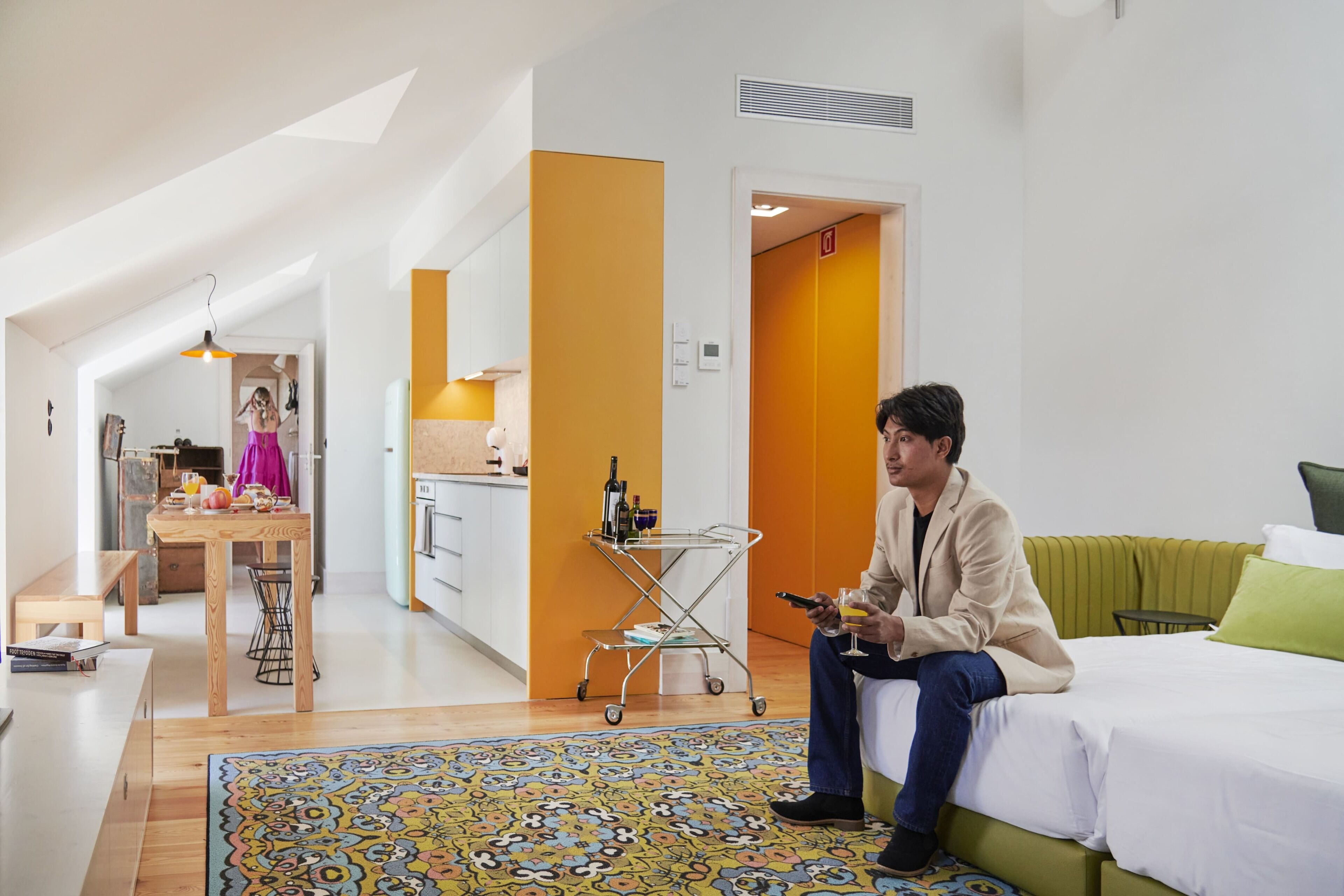 A modern hotel room with a bed, a dining area, and a kitchen.