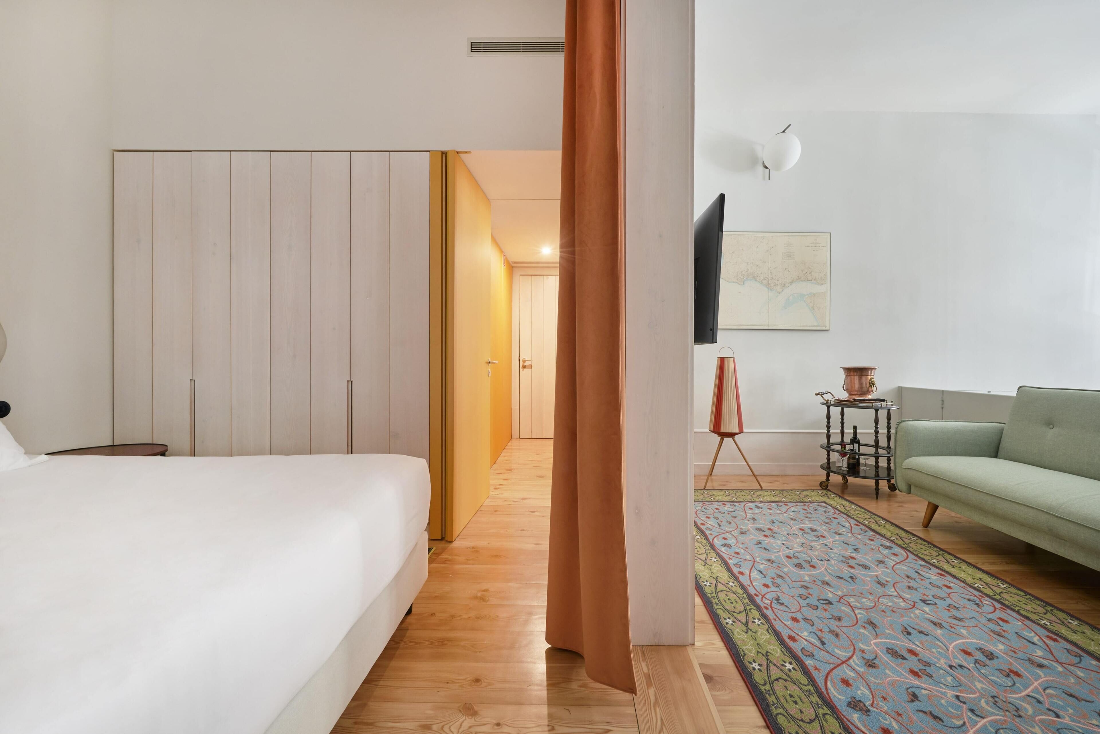 A bedroom with a bed, a wardrobe, a television, a sofa, and a patterned rug.