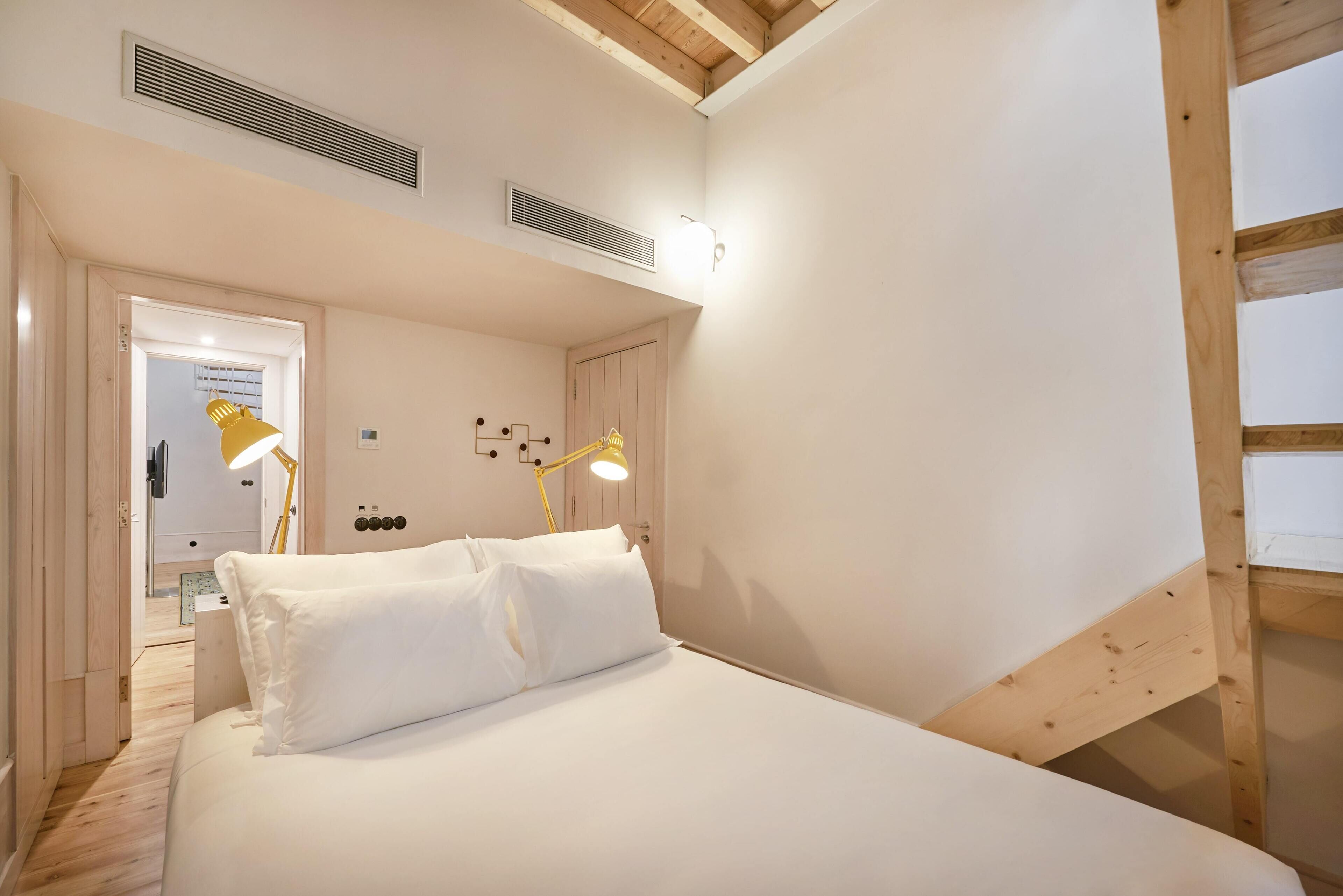 Un dormitorio con una cama, dos lámparas de noche, una puerta y una rejilla en el techo.