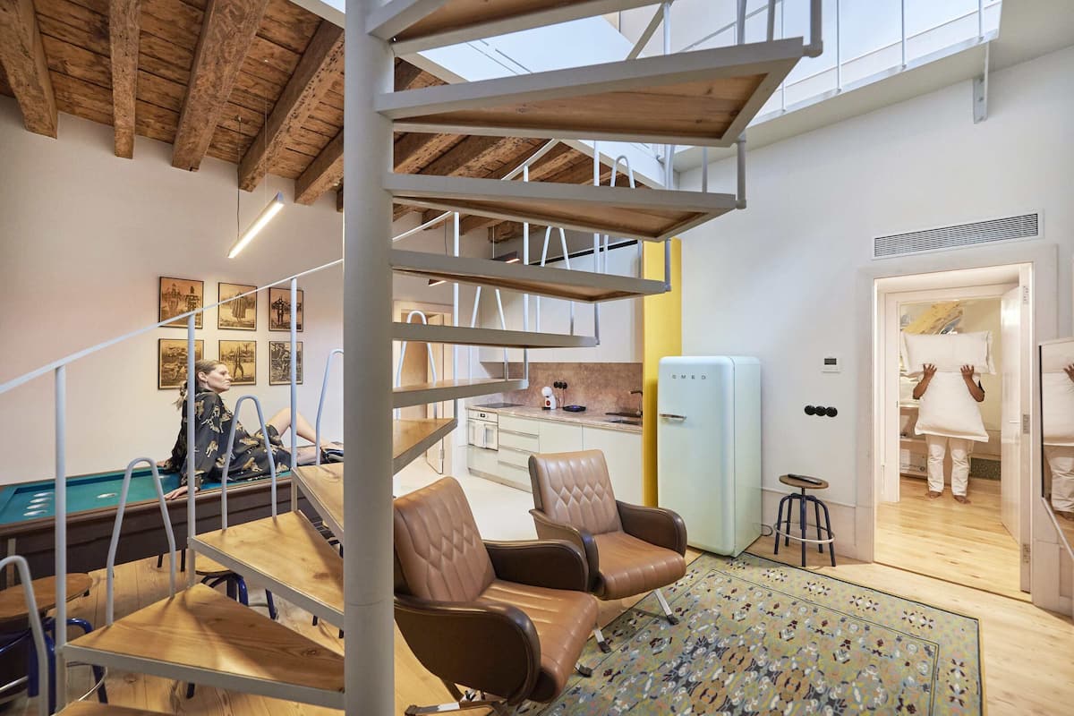 Un interior moderno con una escalera de madera, una zona de estar y una mesa de billar.
