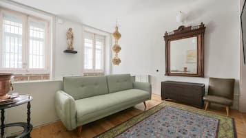 Un salon avec un canapé vert clair, un tapis à motifs, un meuble en bois et un grand miroir.