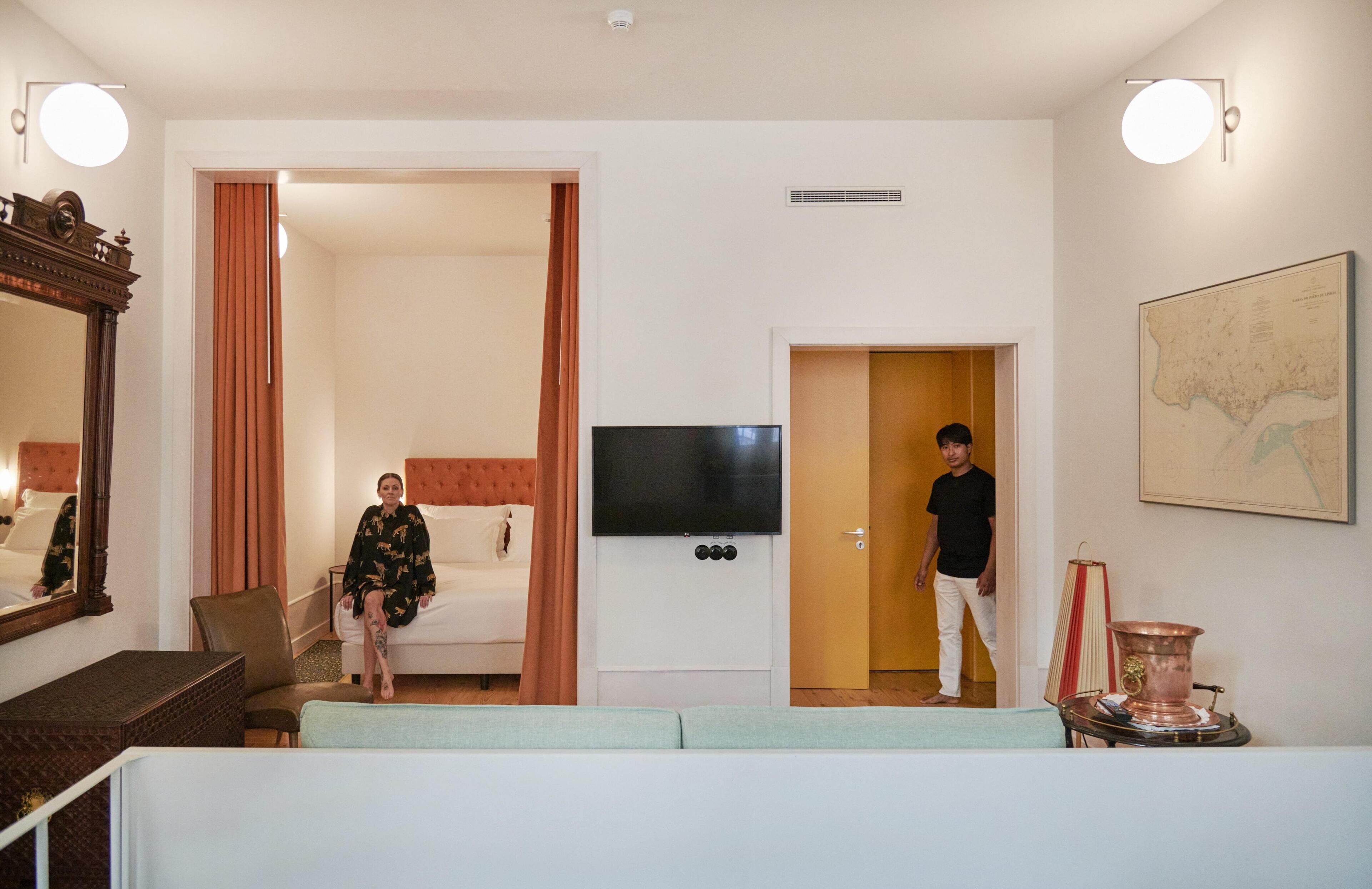 Habitación de hotel con una cama, un televisor, un mapa en la pared y una persona de pie en la entrada.