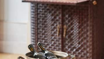 A vintage metal bowl with bottles on a green quilted table, set against a wooden cabinet with shelves of bottles and glasses.