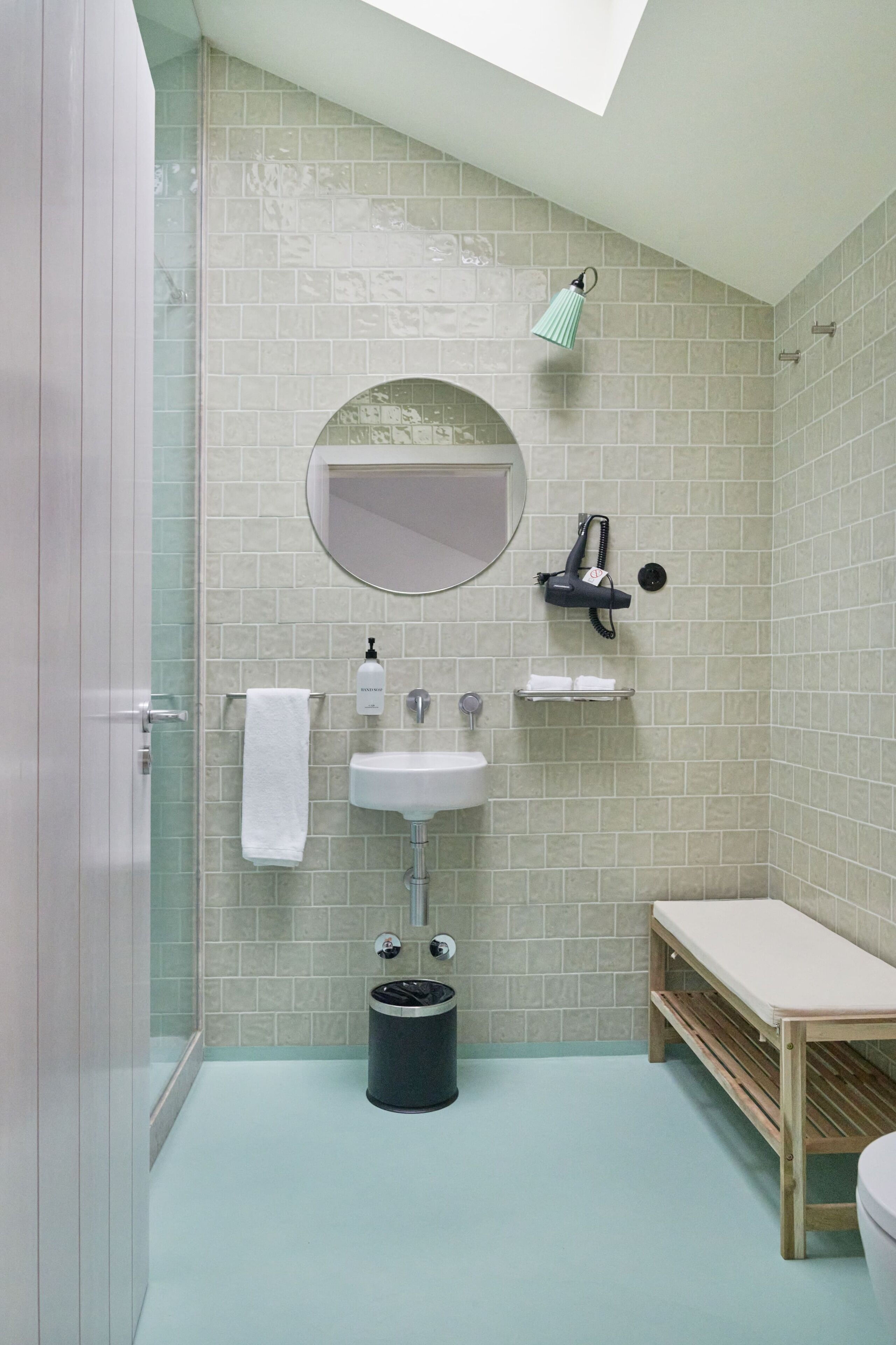 Un baño con lavamanos, espejo, perchero y una mesita.