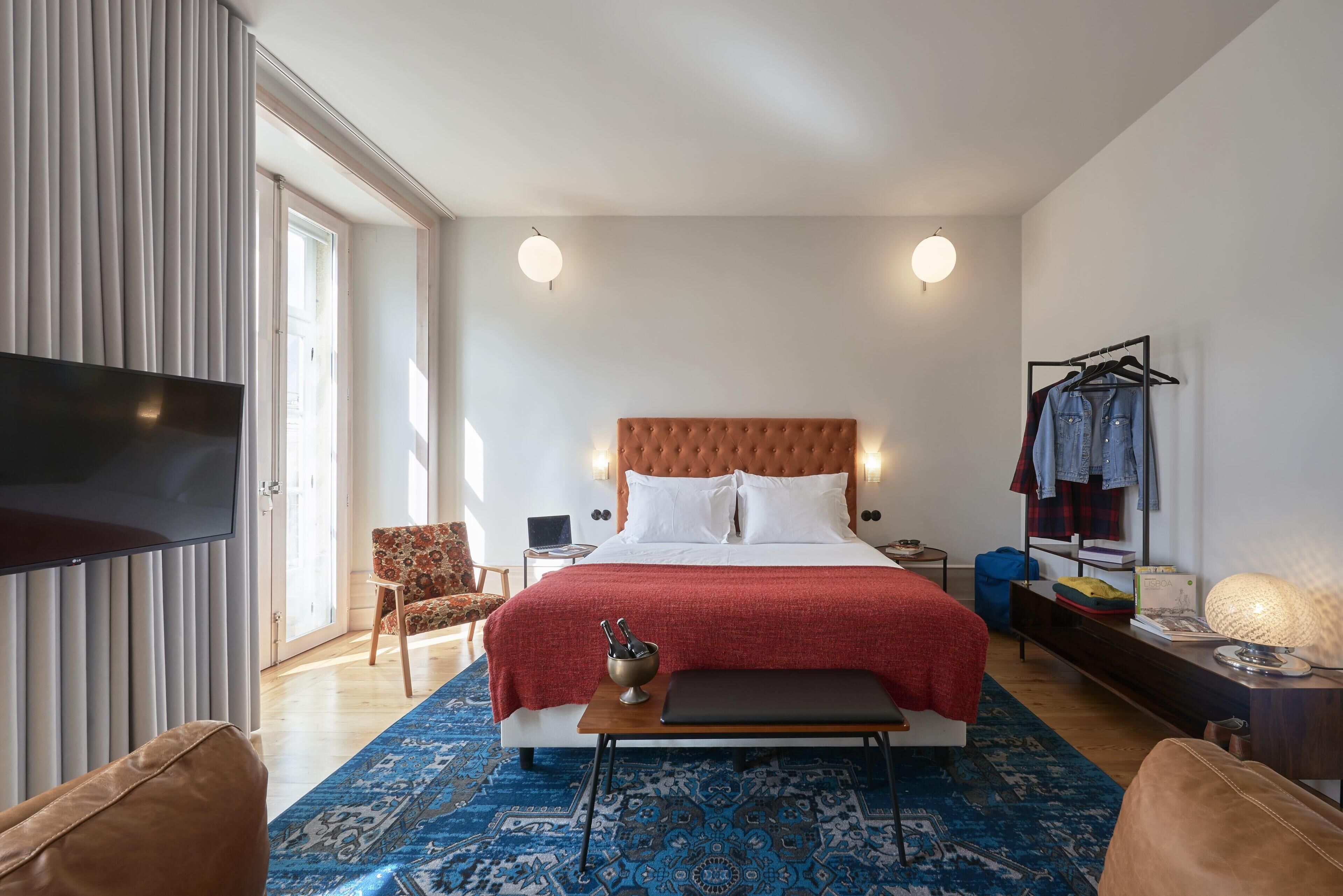 Una habitación de hotel moderna con una cama grande, un televisor de pantalla plana, un escritorio con una computadora portátil, una silla y un armario.