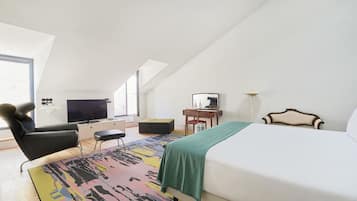 Une chambre d’hôtel moderne dotée d’un grand lit, d’un bureau avec une chaise, d’une télévision et d’une fenêtre laissant entrer la lumière naturelle.