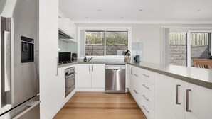 A modern kitchen with white cabinetry, stainless steel appliances, and a wooden floor. - Banksia by the Sea, Gerroa (Gerroa)