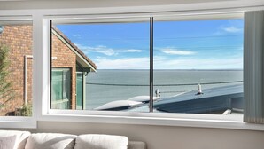 A room with a large window overlooking a body of water and a distant shoreline. - Banksia by the Sea, Gerroa (Gerroa)