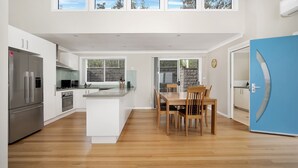 A modern kitchen with white cabinets, stainless steel appliances, and a wooden dining table. - Banksia by the Sea, Gerroa (Gerroa)