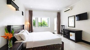 Habitación de hotel con cama, mesita de noche, lámpara, televisor y escritorio con computadora.