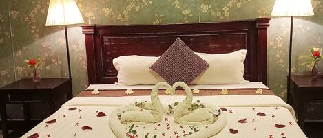 A hotel room with a large bed, floral wallpaper, two bedside lamps, and a decorative swan centerpiece.