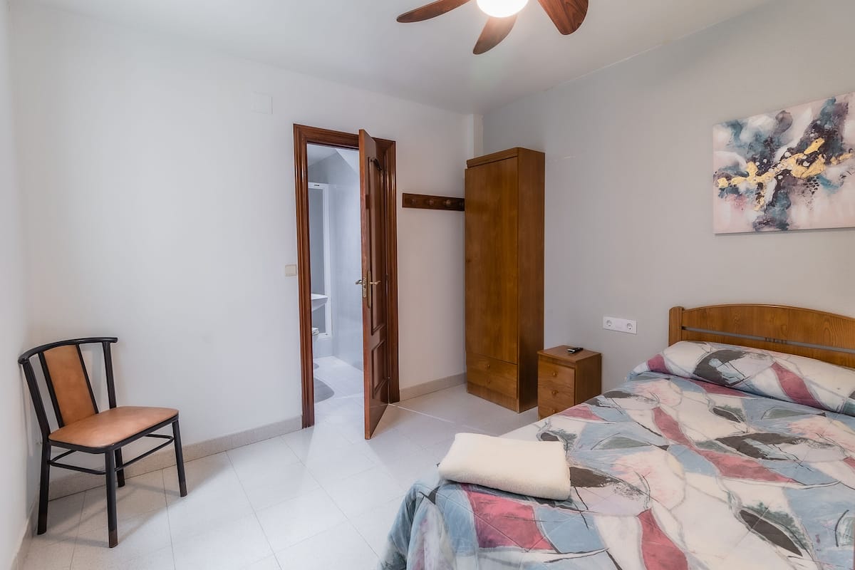 A bedroom with a bed, a chair, a wardrobe, and a ceiling fan.