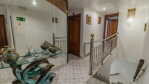 Una escalera con barandilla de cristal, una puerta de madera y un candelabro fijado a la pared.