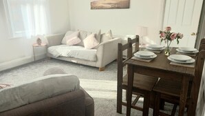 Ett mysigt vardagsrum med en soffa, ett träbord med plats för fyra personer och en tavla på väggen.