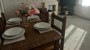 Ett matbord dukat med tallrikar, en vas med blommor och en tv-apparat i bakgrunden.