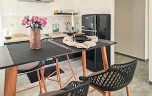 Eine moderne Küche mit schwarzem Arbeitsplatz, Kupferstühlen, einem schwarzen Kühlschrank und einer Vase mit rosa Blumen.