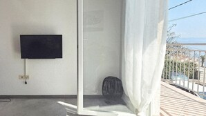 Un balcon avec un téléviseur fixé au mur, une prise de courant et un panier en osier.