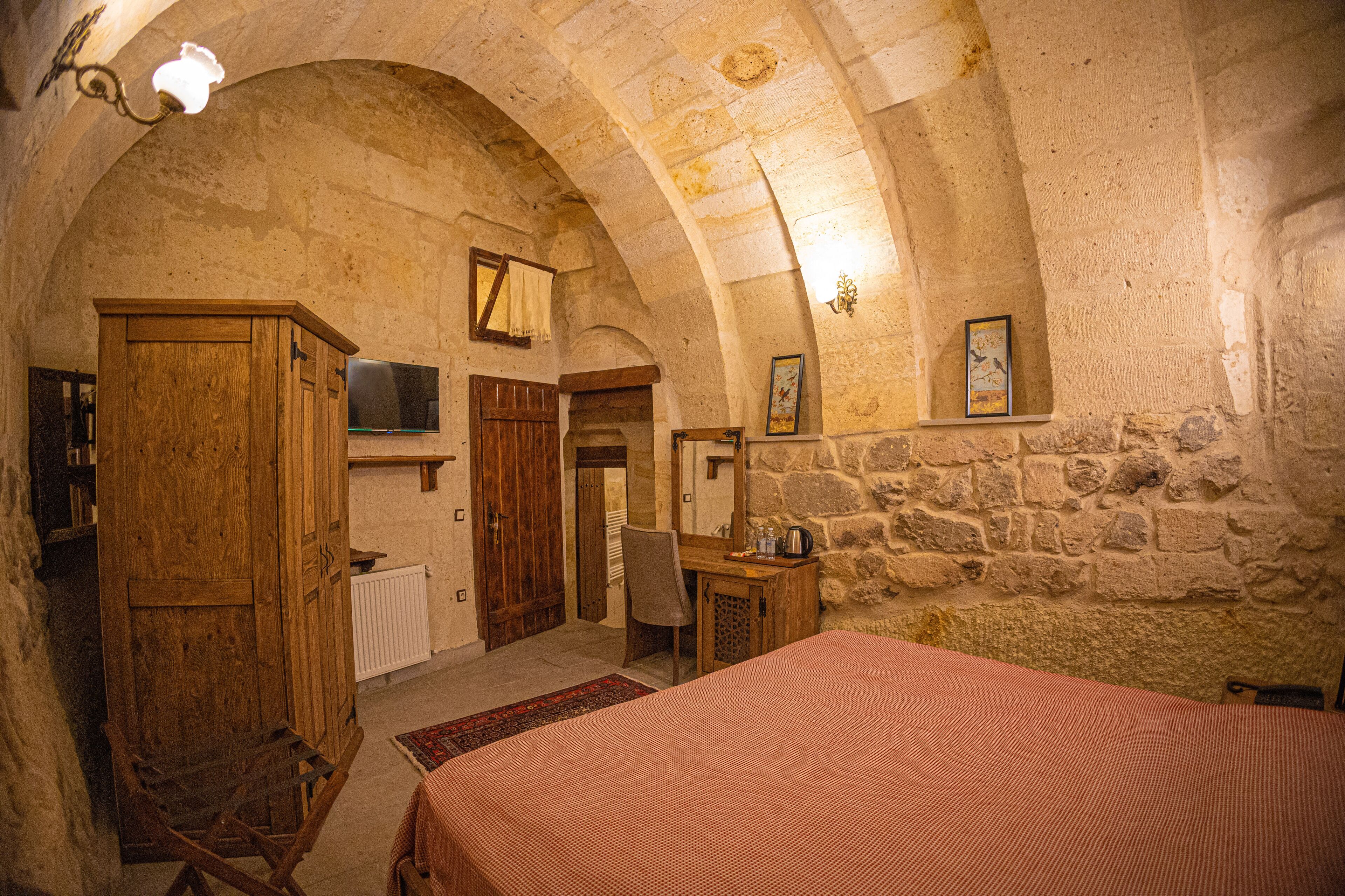 A rustic room with a wooden bed, a desk, a chair, and a stone wall.