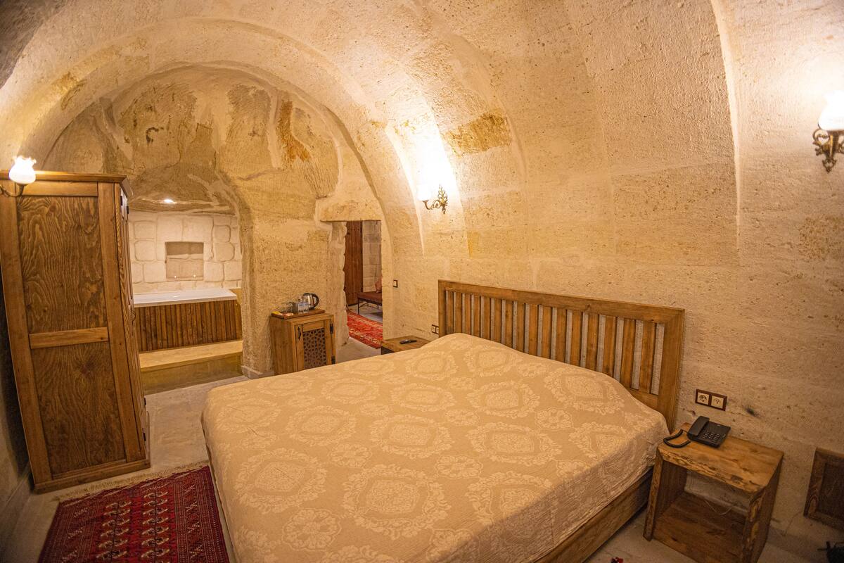 Un dormitorio con una cama de madera, una mesita de noche de madera, una alfombra roja y una pared de piedra.