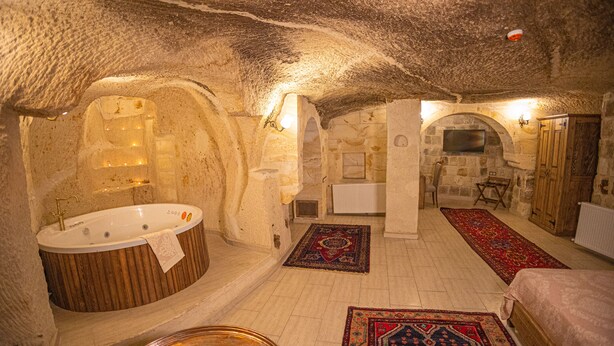 A room with a stone interior, a bathtub, a bed, a wooden cabinet, and a television.