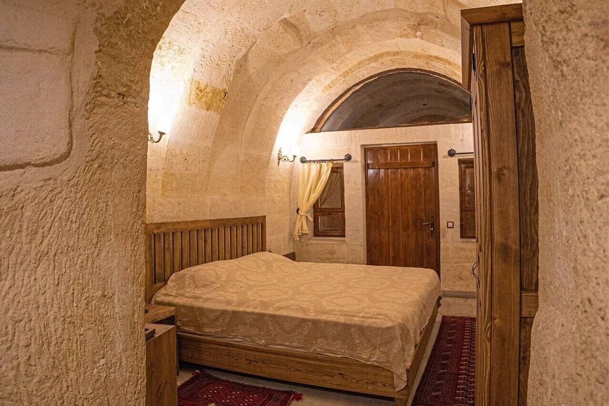 Una habitación con una cama, una puerta de madera y un ventanal pequeño.