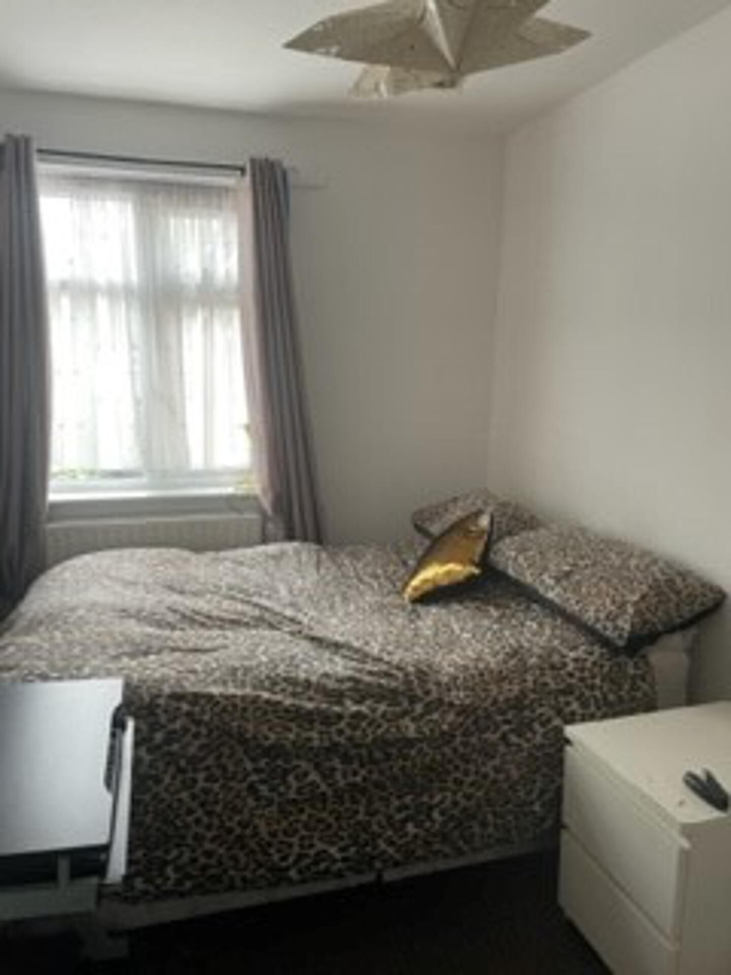 Een kleine, eenvoudig ingerichte kamer met een bed, nachtkastje en een kaptafel.