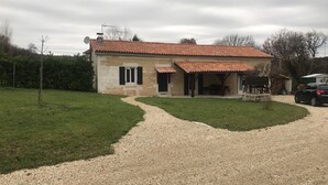 Una casa in pietra con tetto in tegole rosse, vialetto sterrato e prato verde.