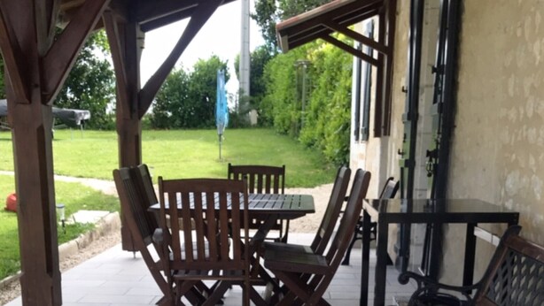 Un portico coperto con pavimento in pietra, tavoli e sedie in legno e una panca.