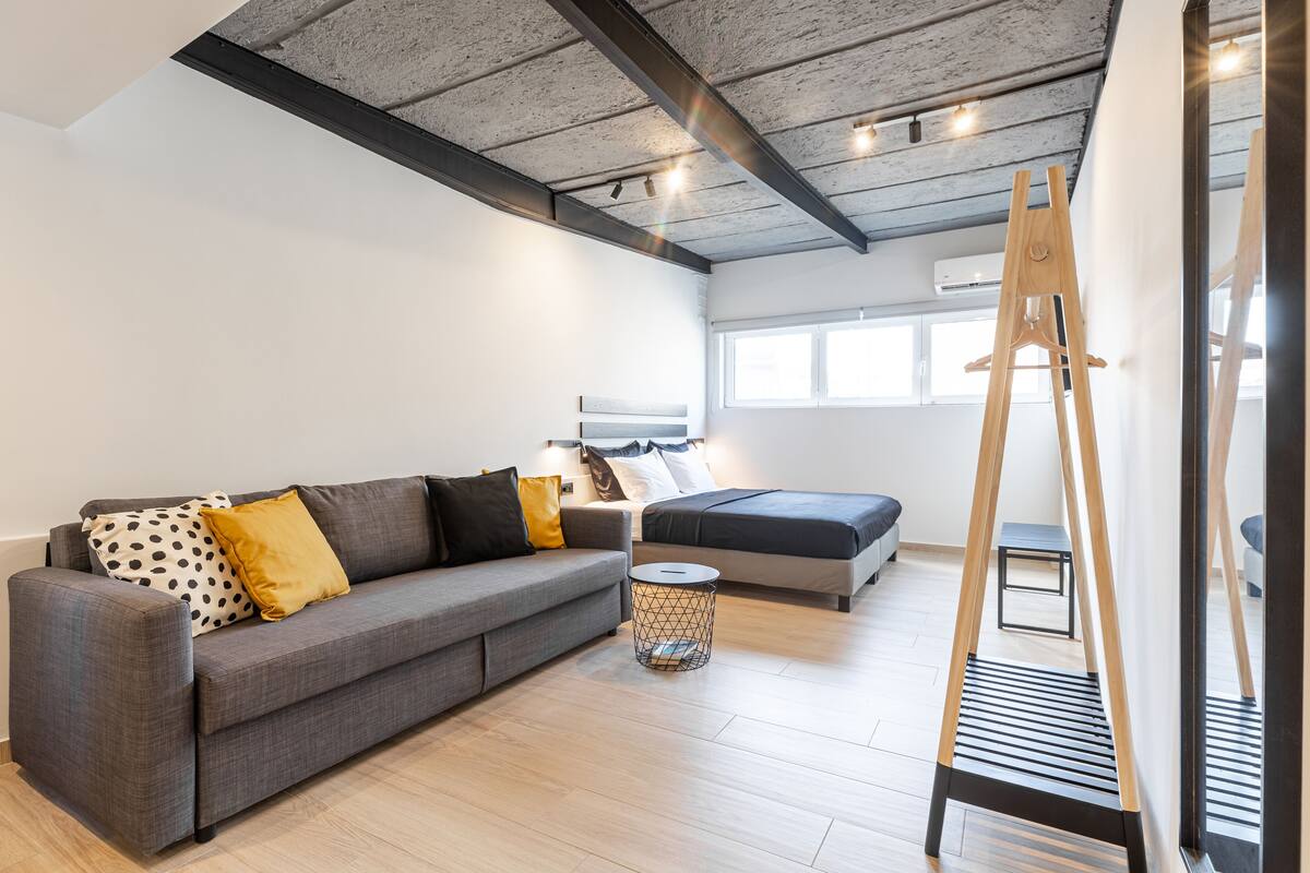 Un salon moderne avec un canapé gris, une petite table d’appoint ronde et une échelle en bois appuyée contre le mur.