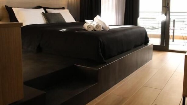 A modern bedroom with a bed, a nightstand, a built-in bench, and a view of the outdoors. - Super Stylish Apartments in the heart of Athens (Athens)