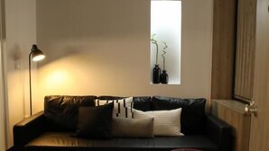 A modern living room with a black leather sofa, a small round table, a floor lamp, and a window with plants. - Super Stylish Apartments in the heart of Athens (Athens)