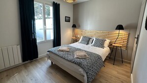 Un dormitorio con cama, ventana con cortinas, lámpara de noche y una lámpara colgante.