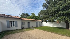 Una casa con camino de grava, un pequeño jardín y una pared blanca con un árbol al fondo.