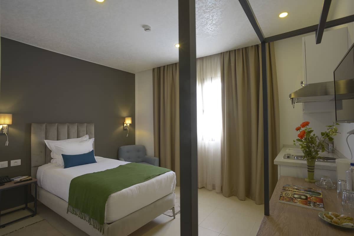 Une chambre d’hôtel avec un lit, une table de chevet, une lampe et un bureau agrémenté d’un vase de fleurs.