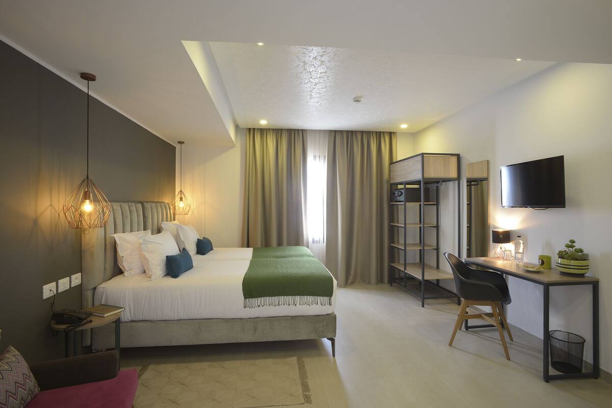 Une chambre d’hôtel moderne équipée d’un lit, d’un bureau, d’une chaise et d’un téléviseur fixé au mur.