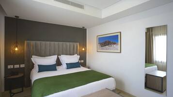 A modern hotel room with a large bed, a bedside table, a mirror, and a picture on the wall.